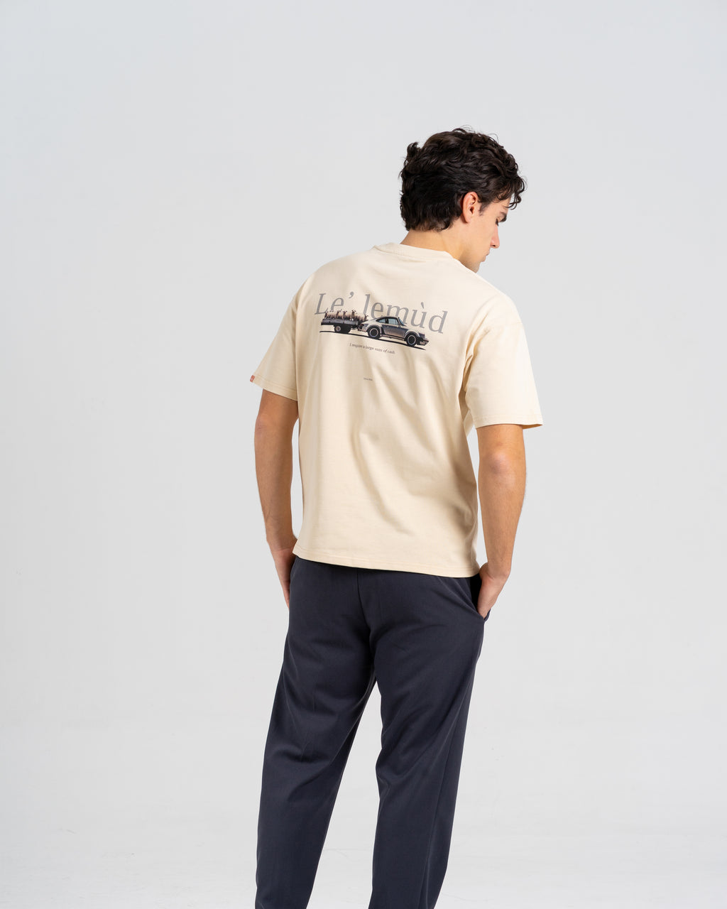 Back view of man wearing Lelemud Economist tee in cream with vintage car graphic print