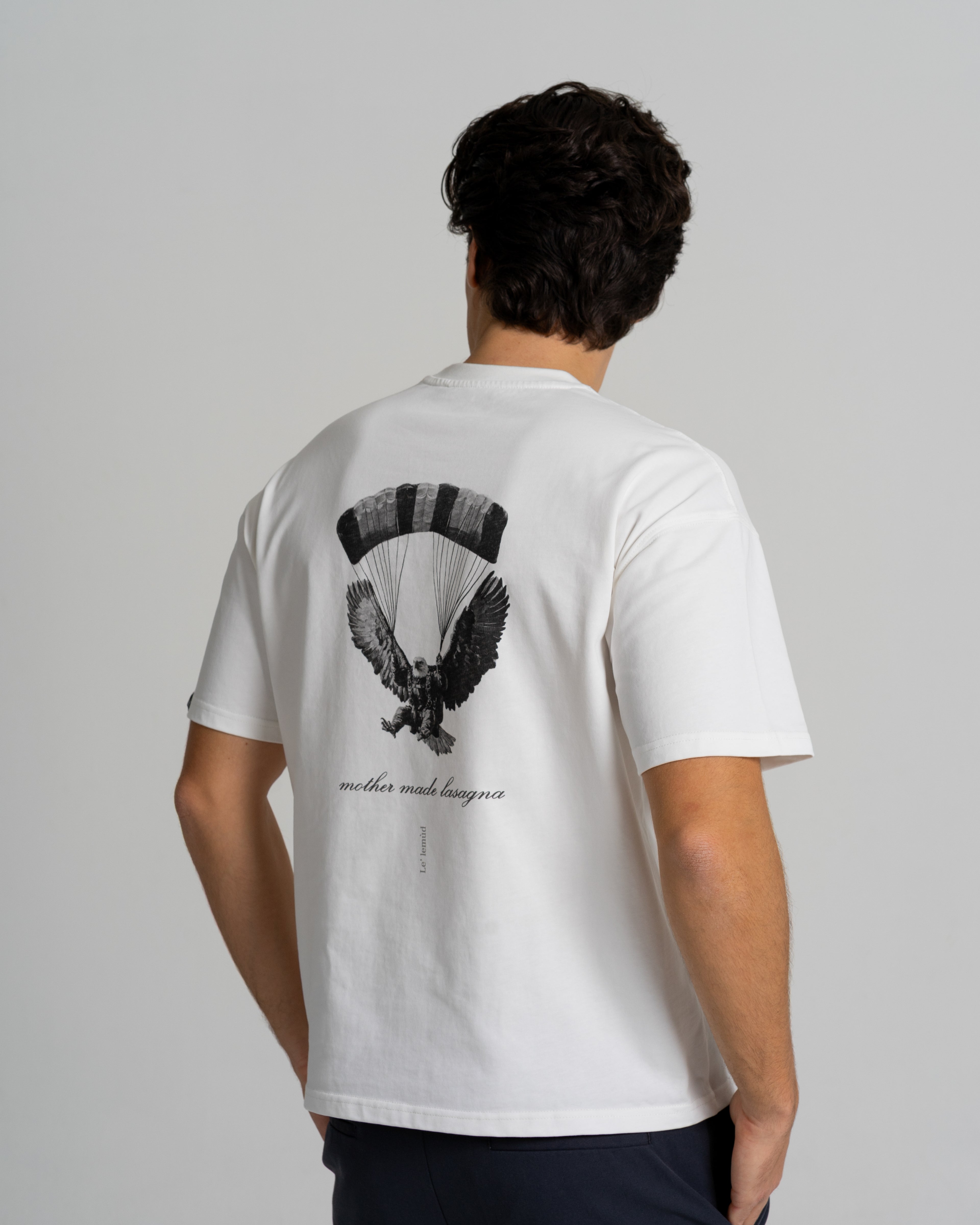 White oversized t-shirt with black eagle graphic on the back by Le Lemud, worn by model, side view, displayed on a white background